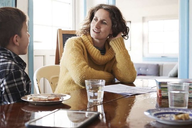 A mother and child sitting at the kitchen table, talking to each other about feelings surrounding chronic illness