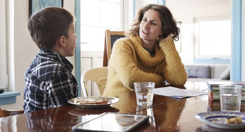 A mother and child sitting at the kitchen table, talking to each other about feelings surrounding chronic illness