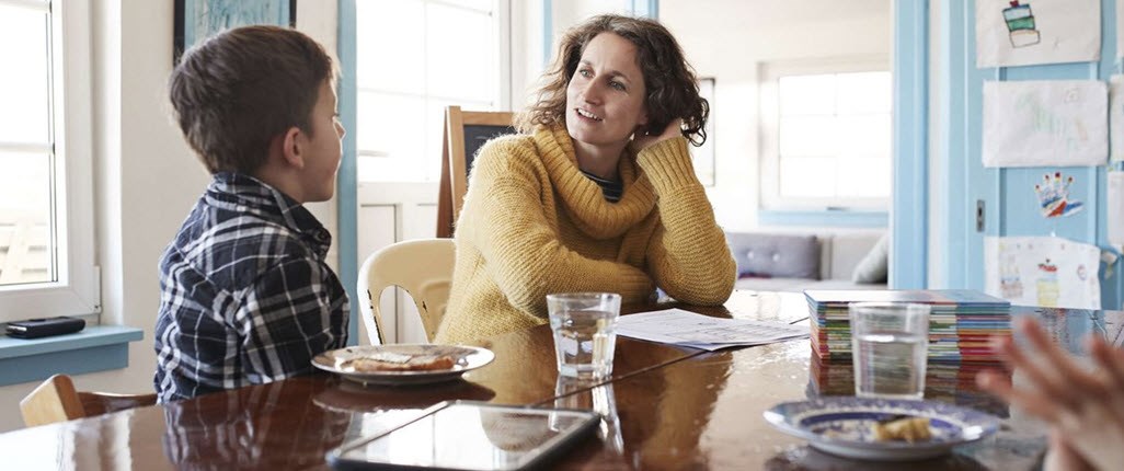 A mother and child sitting at the kitchen table, talking to each other about feelings surrounding chronic illness